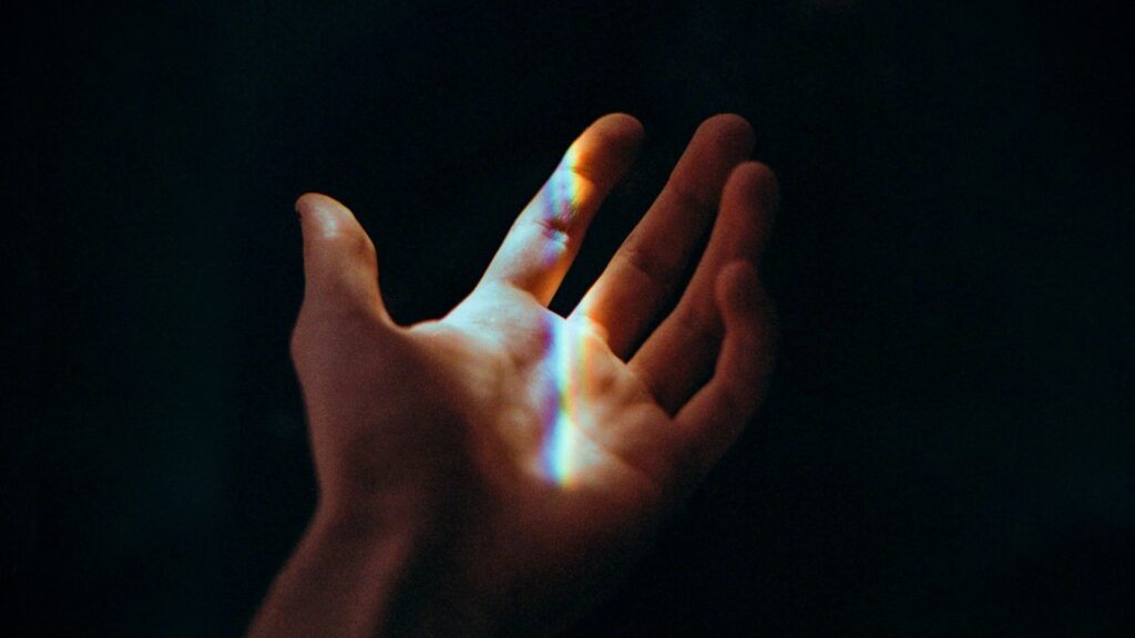 An open human palm reaching upward with a soft rainbow beam of light refractor passing across the hand against a dark background.
Beyond the Retina: Dimensions, Spacetime, and the Reality We Cannot See
