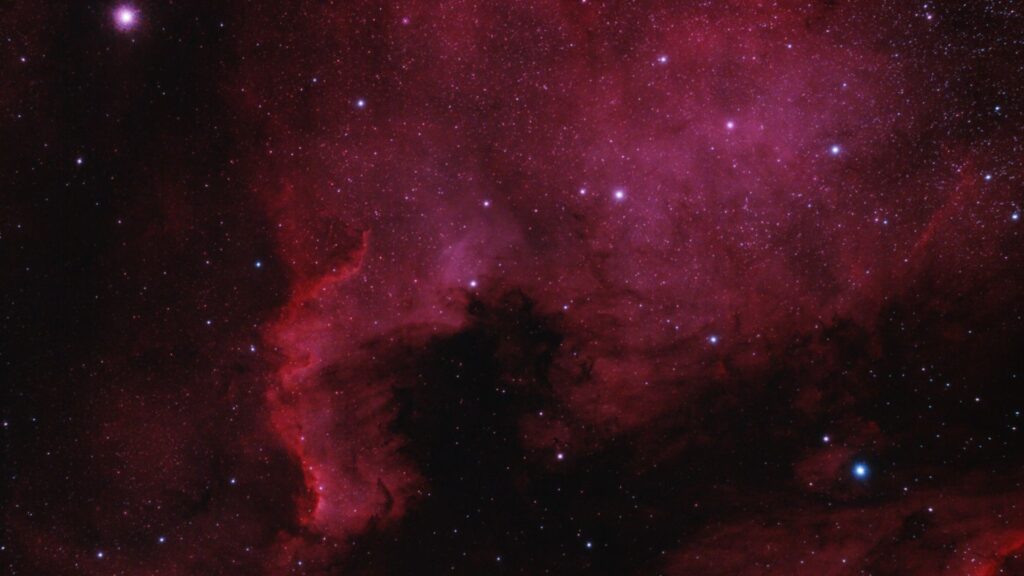 Deep space view of a glowing red and magenta nebula filled with distant stars, representing cosmic space and time